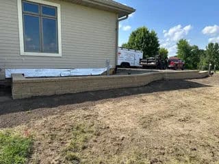 Retaining wall installation beside a home with landscaping preparation in progress.