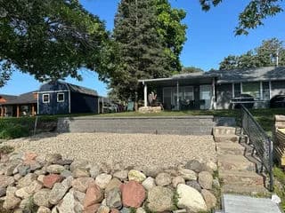 Scenic lakeside property with stone steps, landscaped backyard, and blue sky.