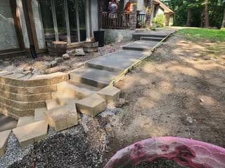 Newly built concrete walkway leading to a house, with stone steps and a grassy area.