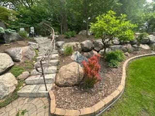 Garden pathway leading up stone steps, surrounded by rocks and lush greenery.